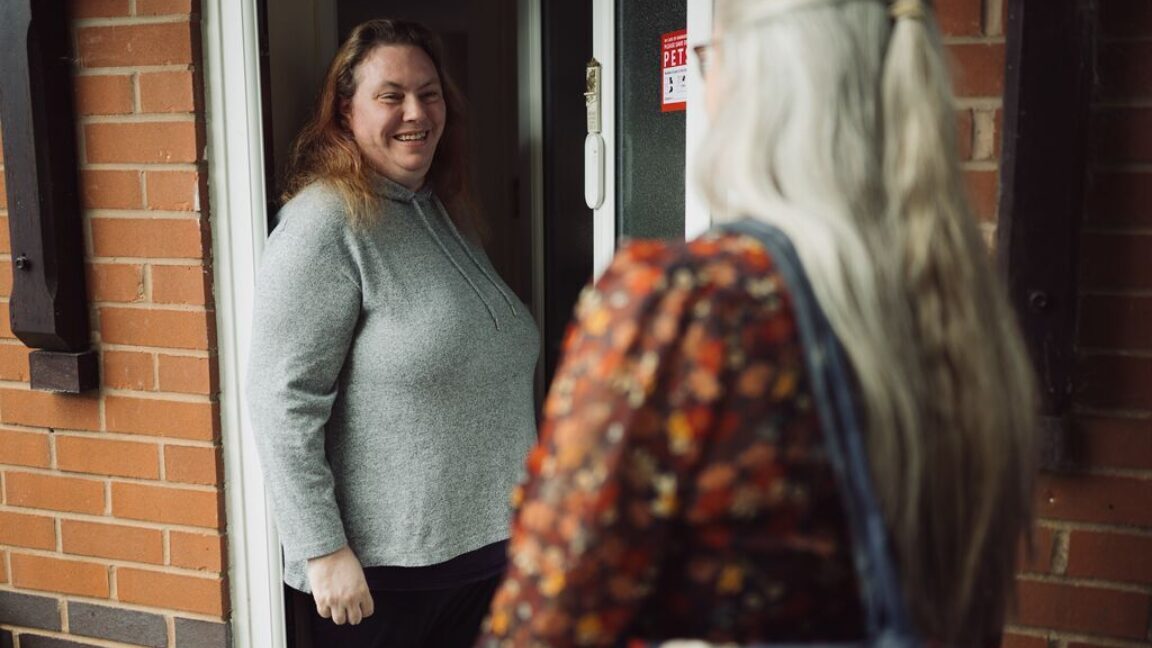Woman standing in doorway, smiling at visiting debt coach
