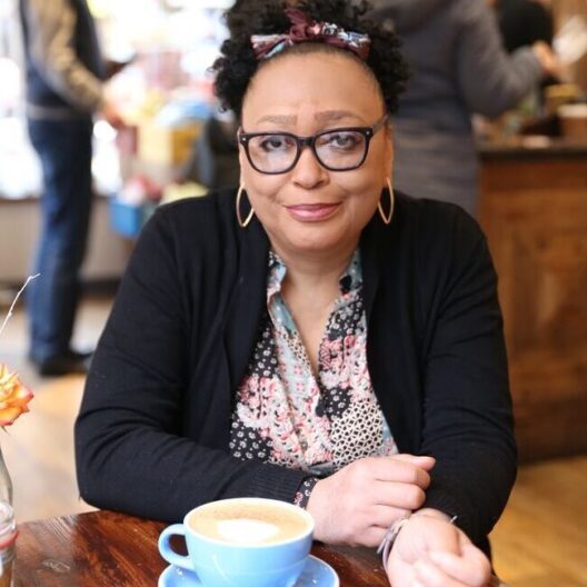 CAP client, Sharon, sat in a coffee shop and smiling directly at the camera