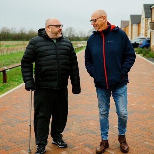 CAP client, Stevie, walking next to his debt coach, Colin, on his street. They are both looking at each other and smiling