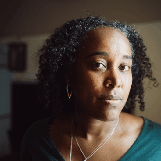 Selene, a black lady with curly black hair, looking at the camera with a serious expression.