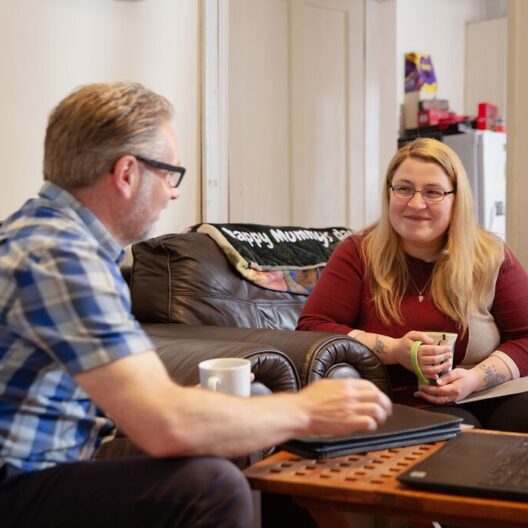 CAP client sat in her living room next to her CAP debt coach, smiling at each other