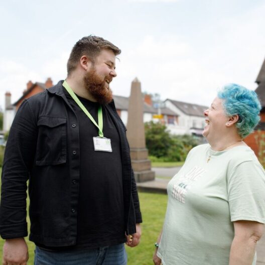 CAP client, Bea, stood outside her local church, smiling at her debt coach, Barney