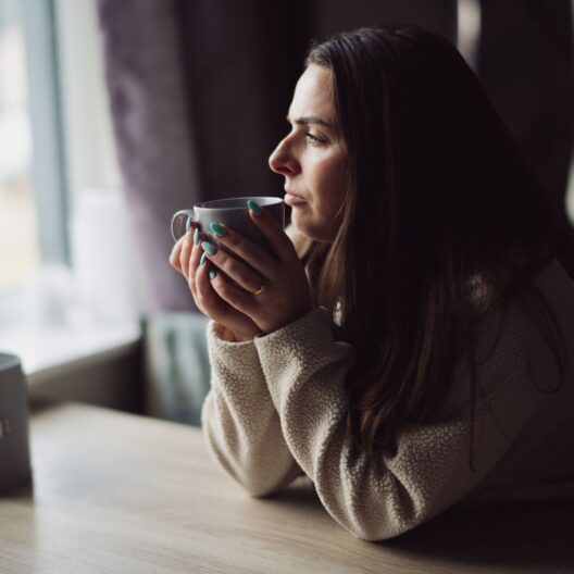 CAP client, Jade, sat at her kitchen table, holding a cup of tea and looking out of her window.