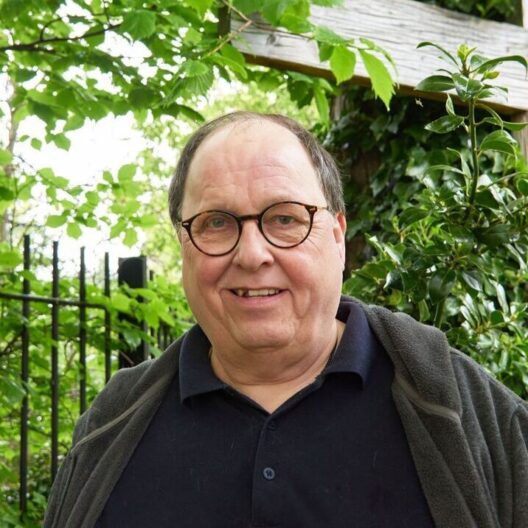 CAP client, Simon, stood outside smiling at the camera, with a large wooden cross propped up against a tree in the background