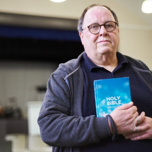 CAP client, Simon, stood inside his local church, looking into the camera and holding the Holy Bible