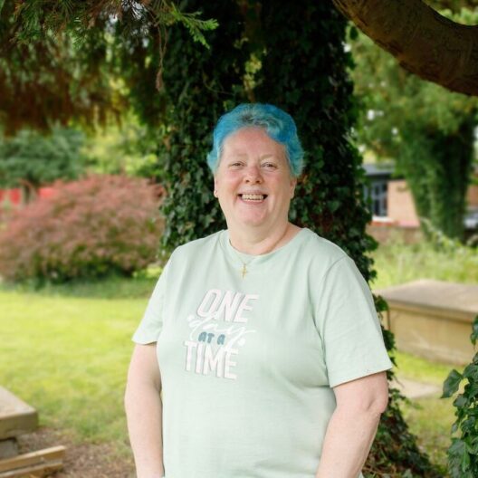 CAP client, Bea, stood outside her local church in their garden, smiling at the camera