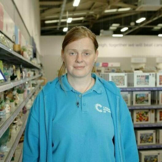 CAP client, stood in a charity shop where she volunteers, smiling at the camera