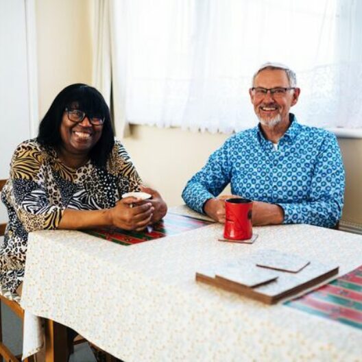 CAP client sat with Debt Coach at a table, drinking a cup of tea and smiling