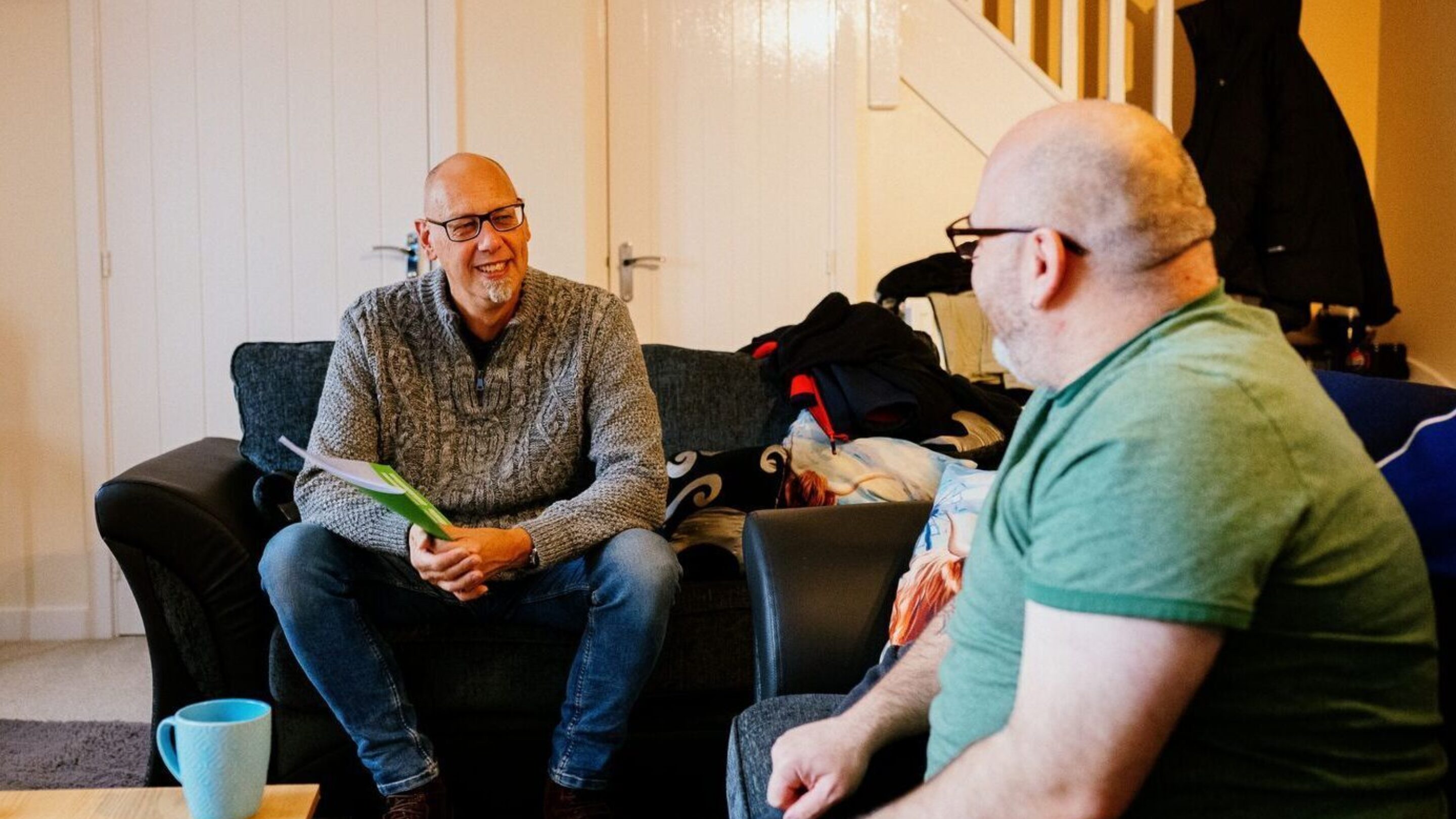 CAP client, Stevie, sat with his CAP debt coach in his living room. They are both looking at each other and smiling