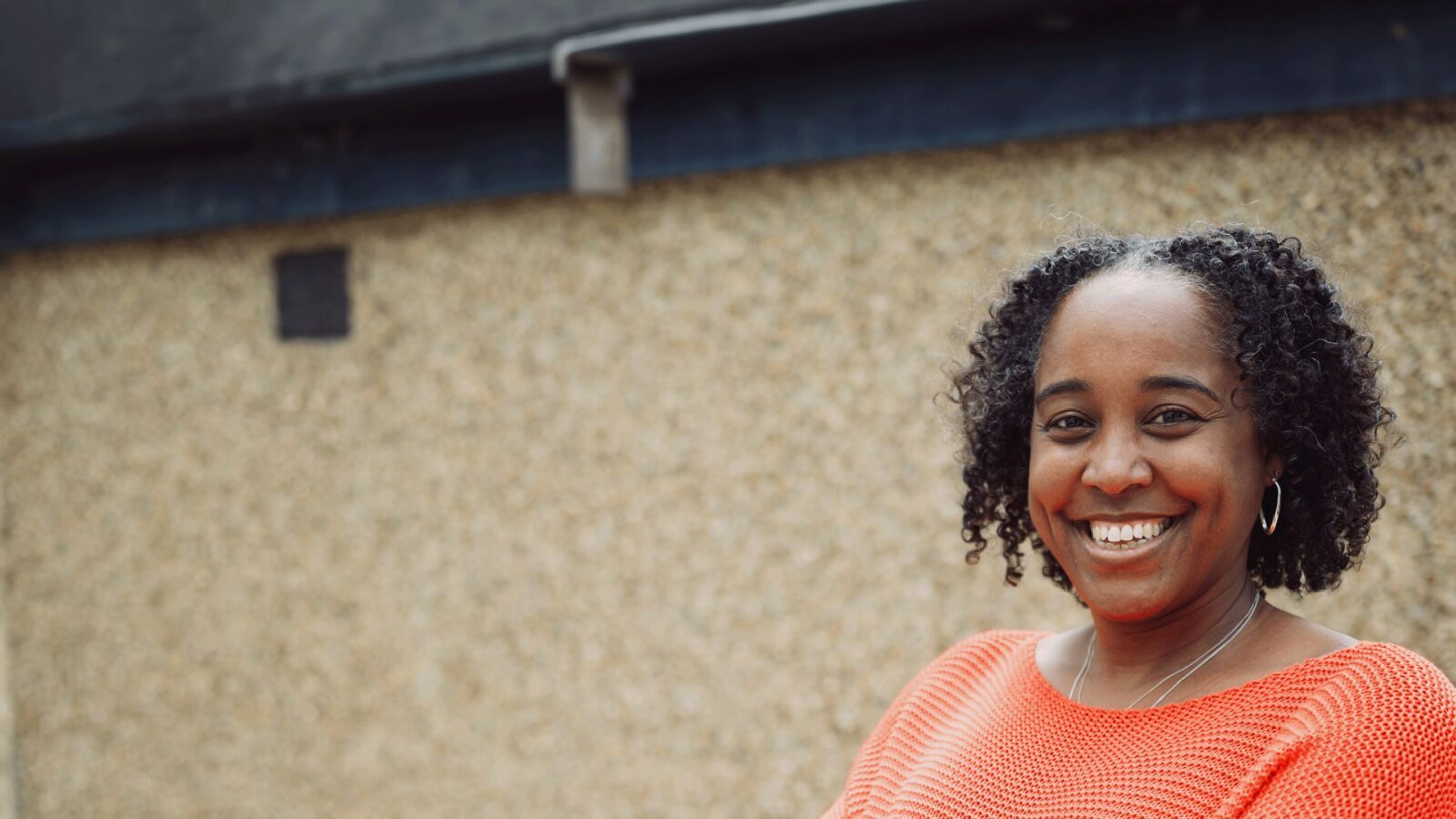 Selene, a Jamaican-Indian woman with brown skin and curly black hair. She is smiling straight at the camera.