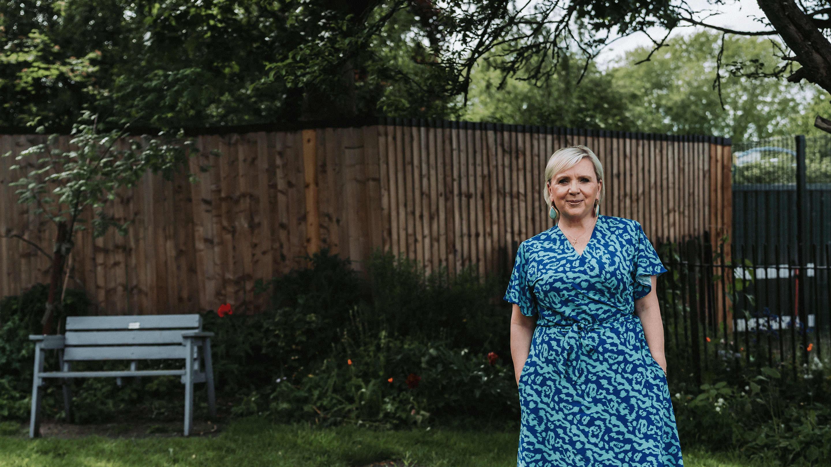 A lady in a blue dress in a garden, smiling at the camera