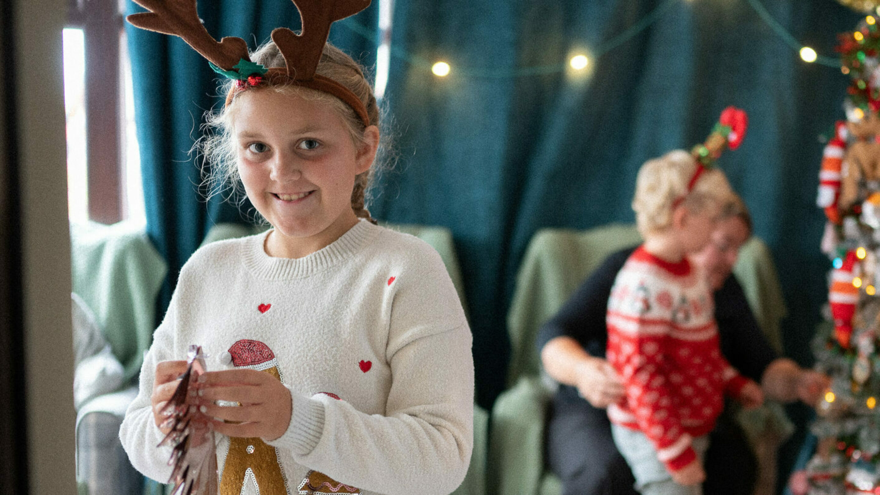 A smiling child, stood in front of a christmas tree