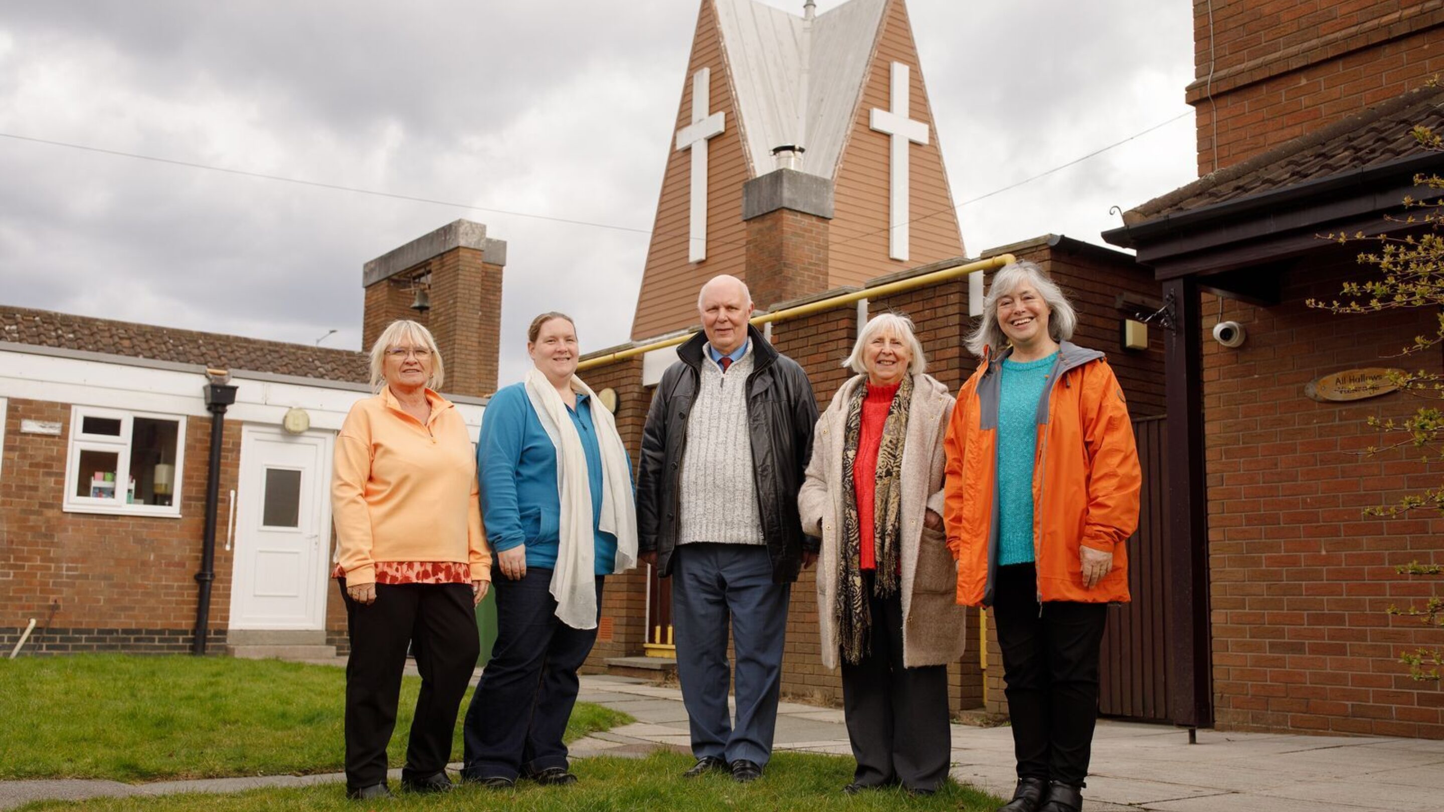 Five middle aged people stood outside their local church, all smiling at the camera
