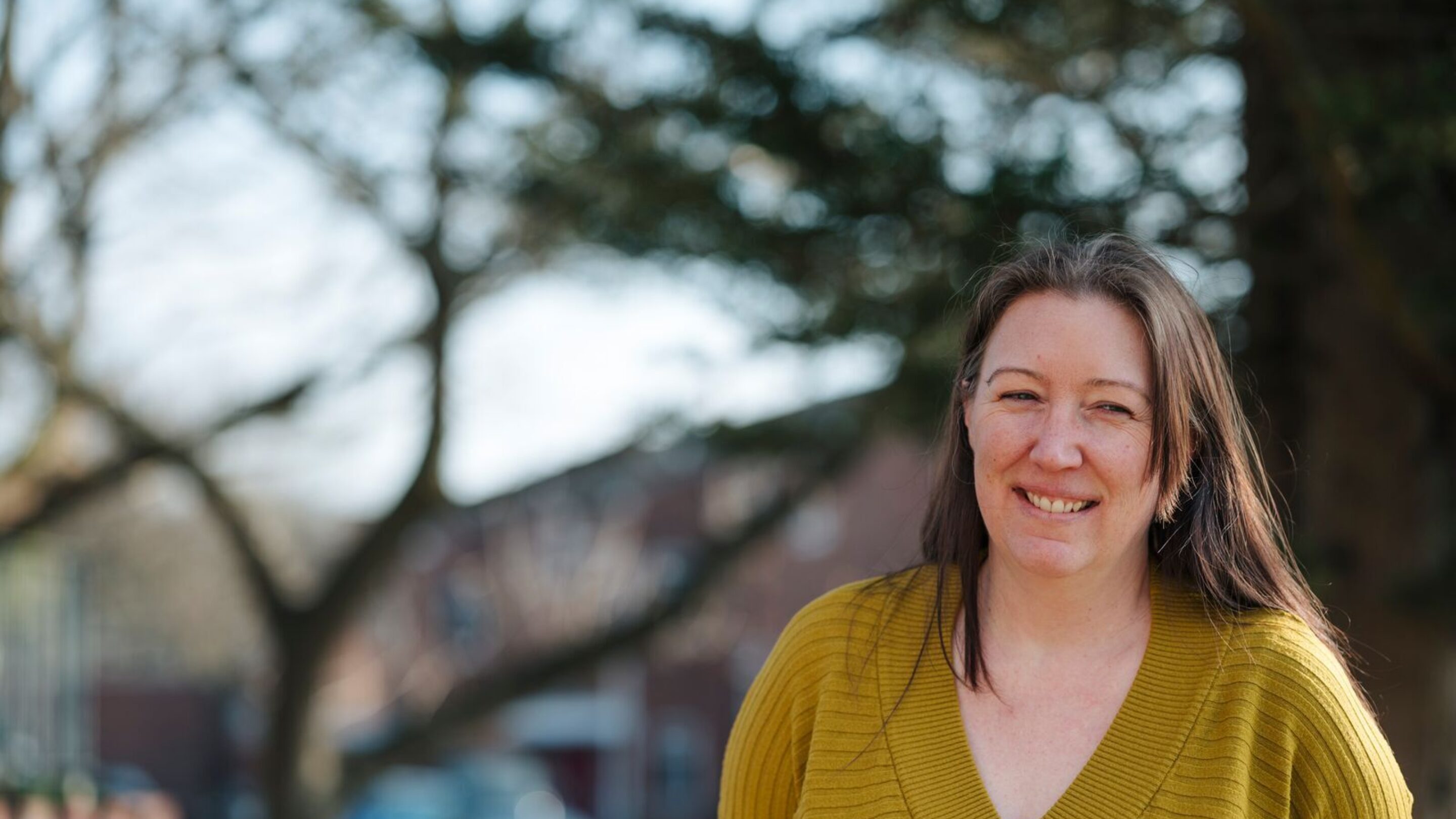 CAP client stood outside, smiling at the camera and wearing a yellow jumper
