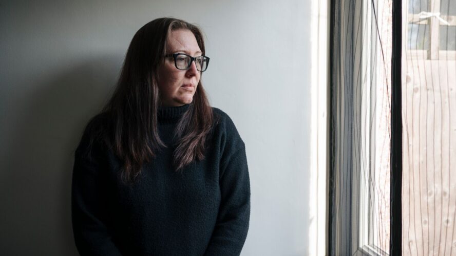Image of a CAP client stood in front of a grey wall, looking out of her window