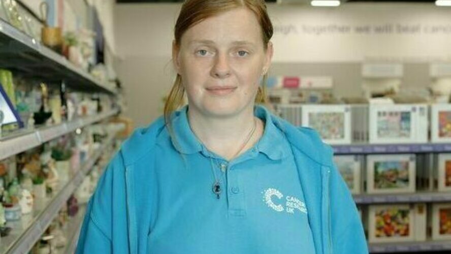 CAP client, stood in a charity shop where she volunteers, smiling at the camera