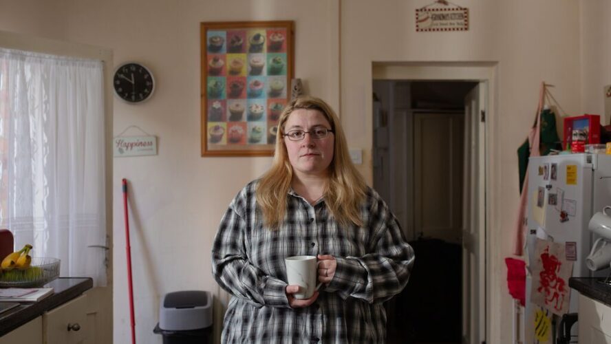 CAP client stood in her kitchen, holding a mug and looking at the camera