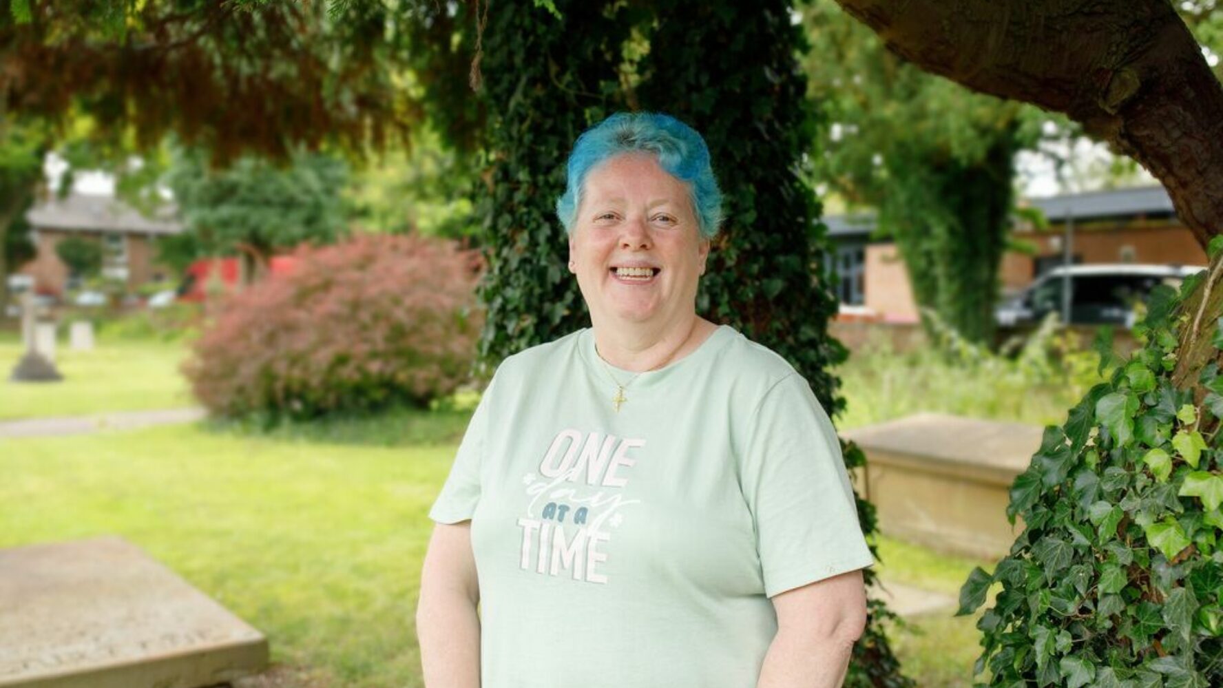 CAP client, Bea, stood outside her local church underneath a tree, smiling at the camera