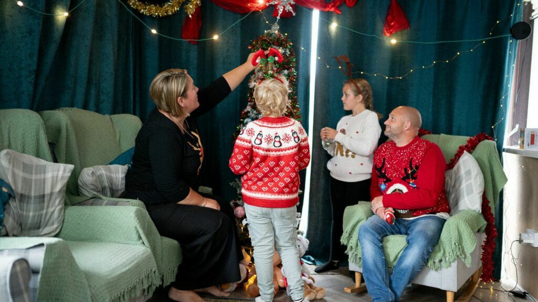 A family of two adults and two children, decorating a Christmas tree in their living room