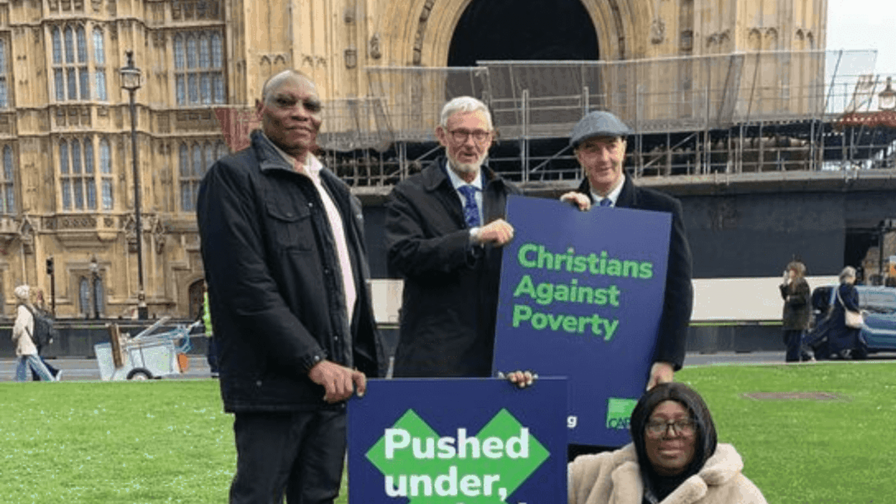 Four CAP storytellers standing outside Westminster, holding signs that say 'Pushed under, pushed out' and 'Christians Against Poverty' as part of CAP's 'Pushed under, pushed out' campaign