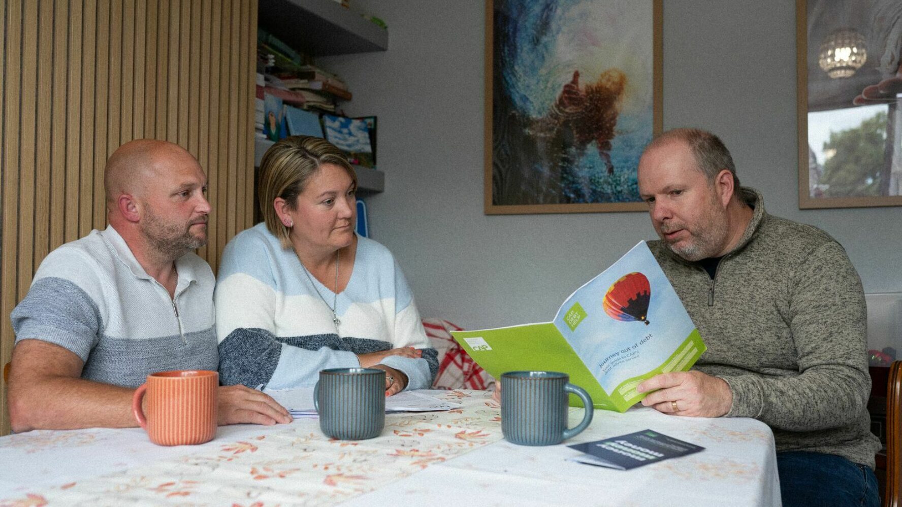 Two CAP clients sat at their dining table with their debt coach, looking at a debt plan leaflet