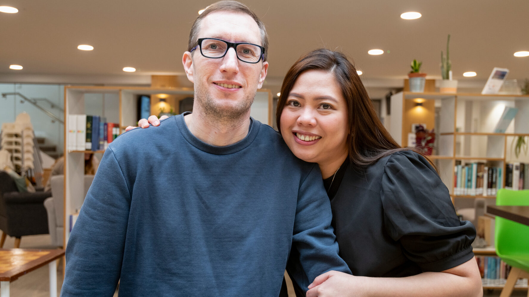 Husband and wife CAP clients at their local job club, hugging each other and smiling directly into the camera
