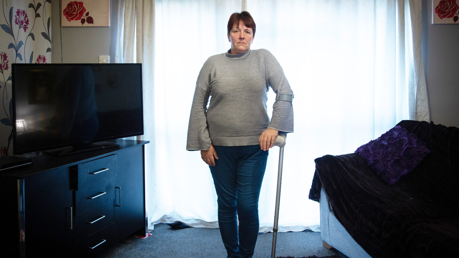 Tina, CAP client, standing in her living room using her crutch on her left arm