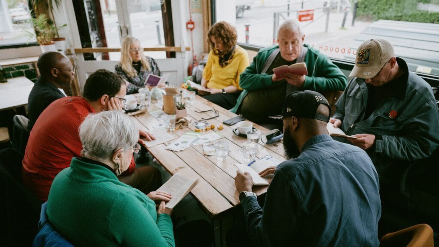 Community group sat around a table in a local cafe, reading the gospel of Luke