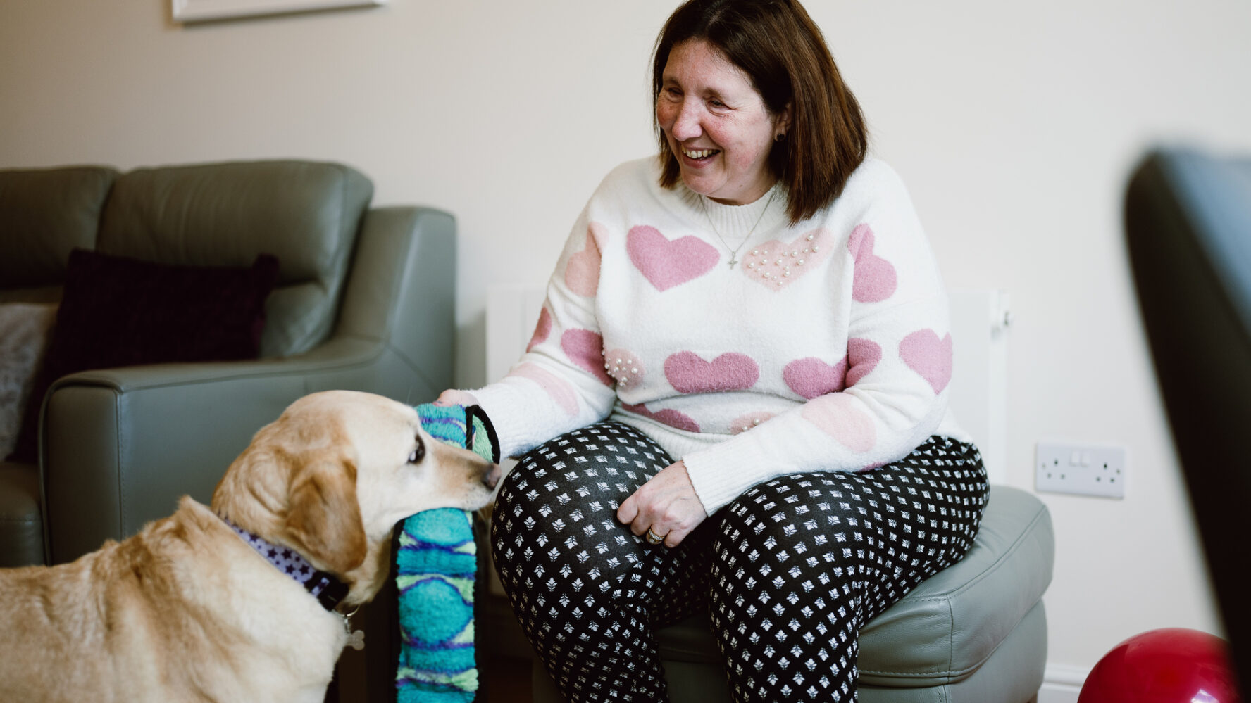 Angela, who lives with sight loss, smiling as she plays with her guide dog