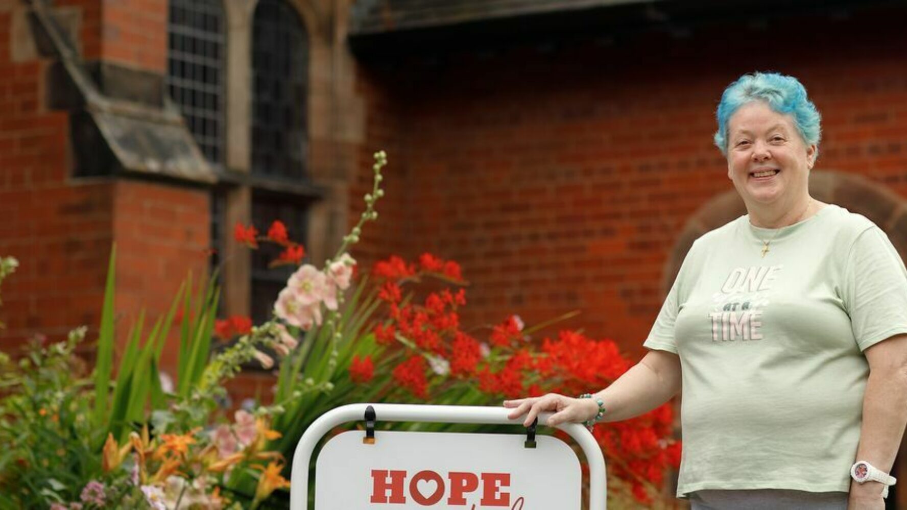 CAP client, Bea, stood outside CAP debt centre, next to sign that reads 'hope'