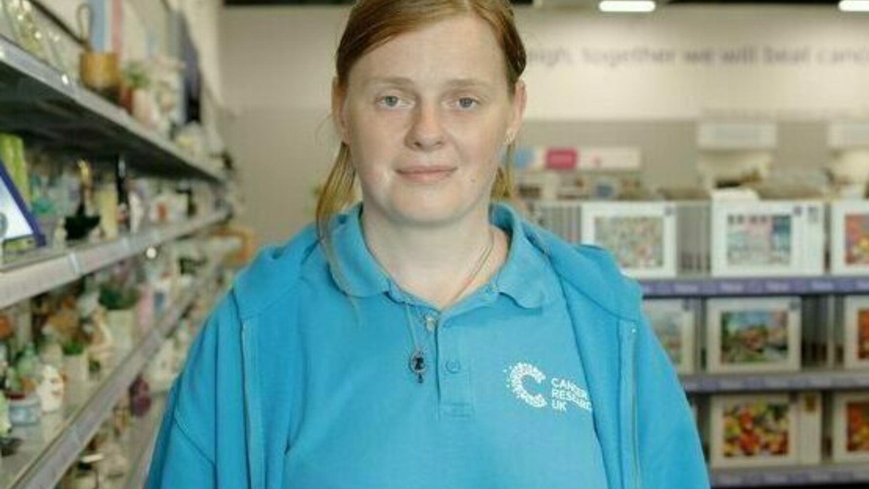 CAP client, stood in a charity shop where she volunteers, smiling at the camera