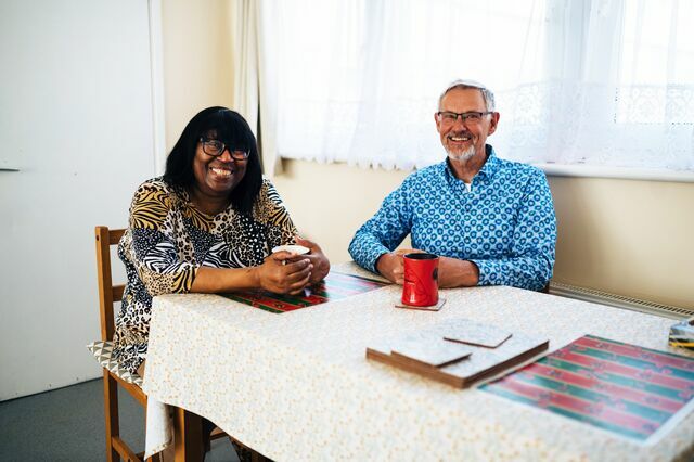 CAP client sat with Debt Coach at a table, drinking a cup of tea and smiling